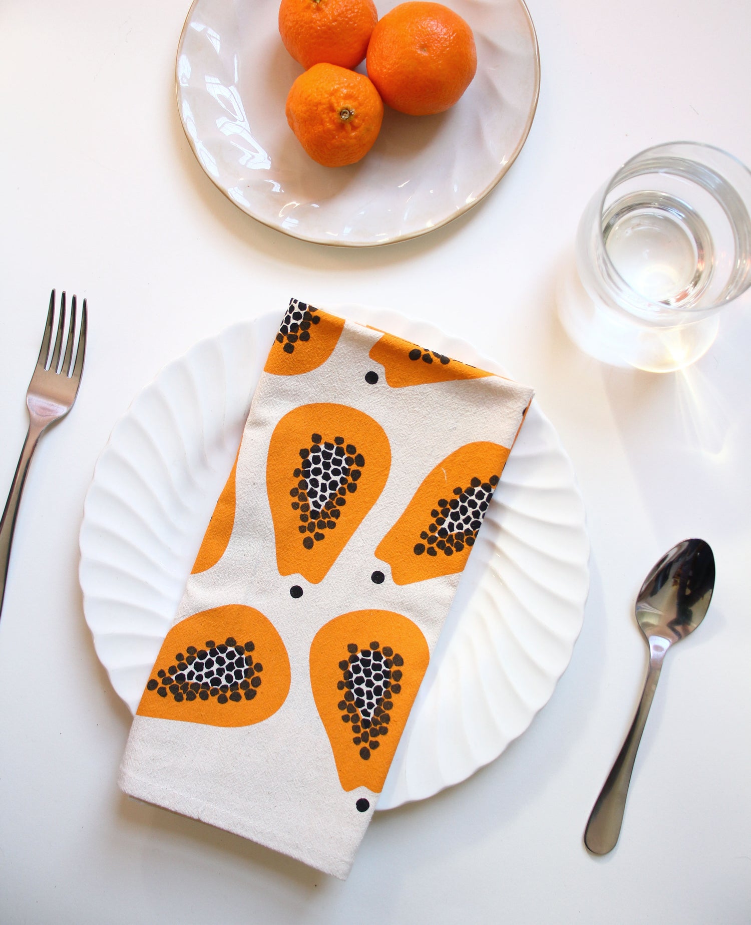 Folded Papaya Pattern Tea Towel on a table top with a plate of oranges